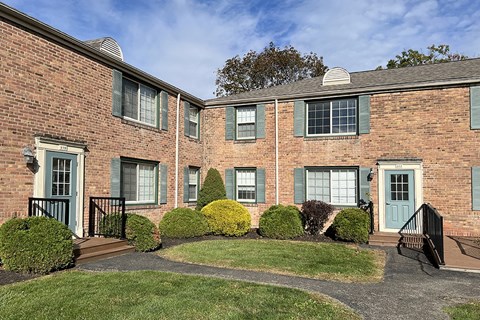 A brick building with green shutters and bushes in front.