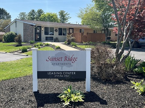 A sign for Sunset Ridge Apartments leasing center stands in front of a building.