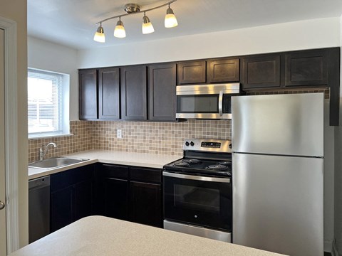 A kitchen with black cabinets and a stainless steel refrigerator.
