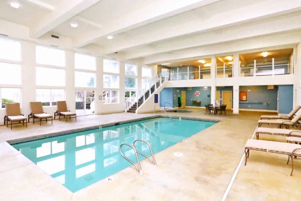 A large indoor swimming pool with lounge chairs and a staircase  at Everett Senior Community, 98201