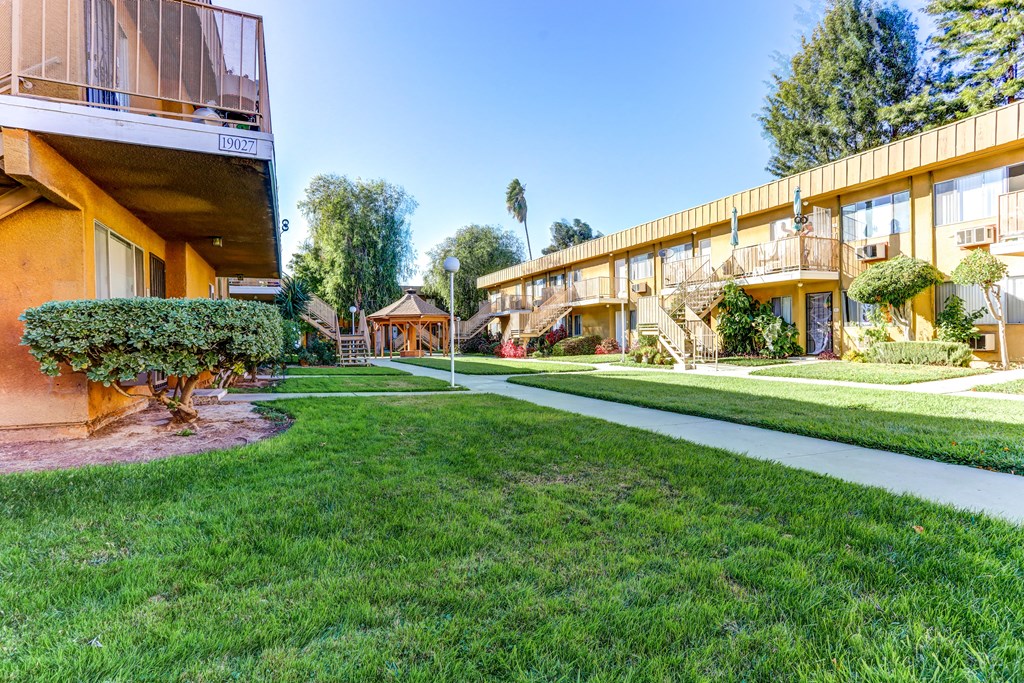 a sidewalk in front of a building with green grass and trees