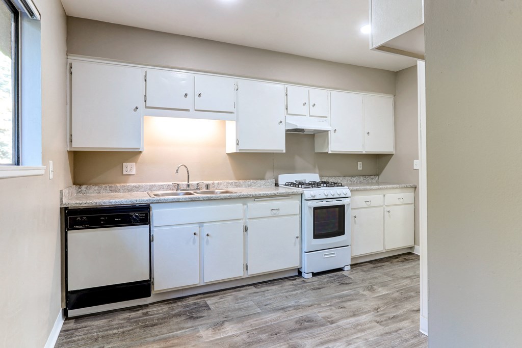 an empty kitchen with white cabinets and appliances and a window