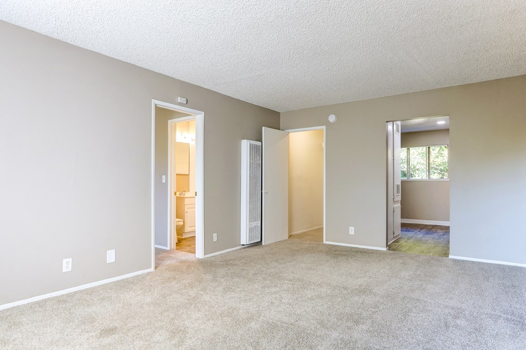 an empty living room with open doors to a bedroom and a bathroom
