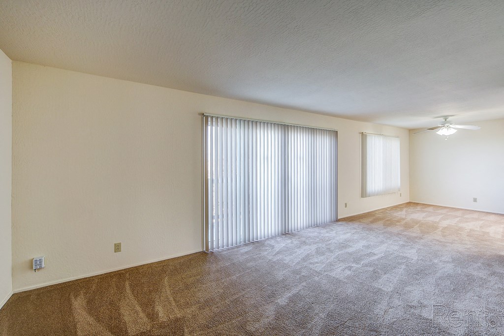 an empty living room with a sliding glass door and a ceiling fan