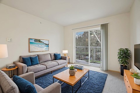 A living room with a grey couch, a blue rug, a wooden coffee table, and a painting on the wall.