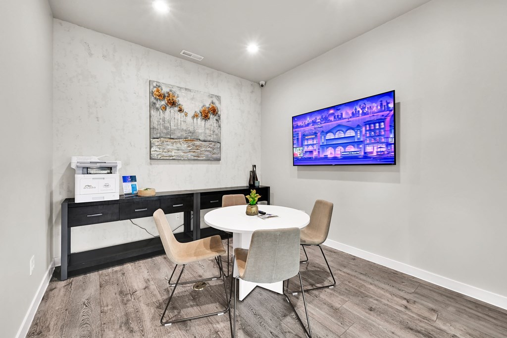 A room with a white table and chairs, a painting on the wall, and a TV screen showing a cityscape.