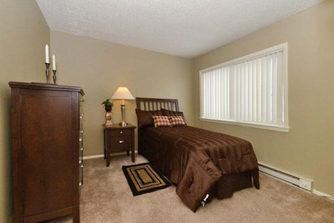 A bedroom with a bed, nightstand, lamp, and a wooden armoire.