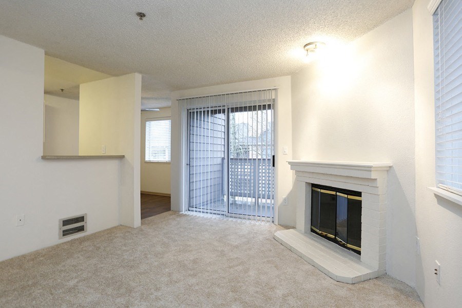 Apartments For Rent In Des Moines - Marina Club - Living Room With Carpet Flooring, A Fireplace, And A Sliding Glass Door Leading to the Balcony Area