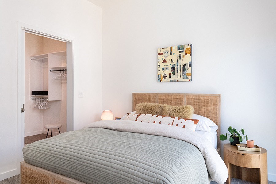 1 BR Apartments in Downtown Sacramento CA - The Mansion - Bedroom with Bed, Carpetted Floor, Wooden Nightstand, Lamps, Large Closet, and Wall Art on White Walls