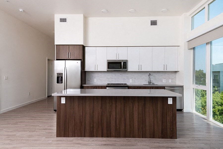 Studios in Downtown Sacramento CA - The Mansion - Modern Kitchen with Stainless Steel Appliances, Wooden and White Cabinets, Gray Counters, Tile Backsplash, Wood Floor, and Large Windows