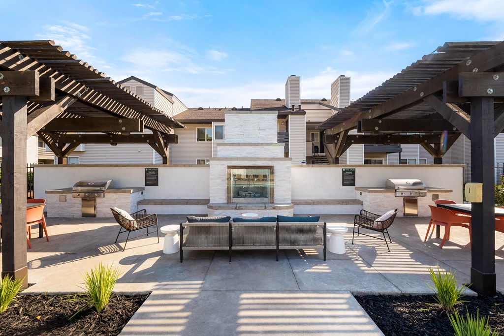 Citrus Heights Apartments for Rent - The Arlo - BBQ Area with Two Grills, Tables, Chairs, a Cozy couch, and a Fireplace