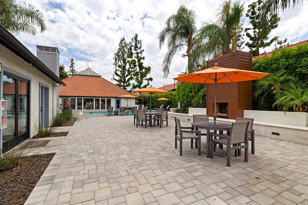 a patio with tables and umbrellas and a pool in the background