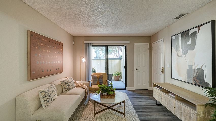 Hayward CA apartments - Austin Commons - wood flooring, white couch with decorative pillows, beige rug, coffee table, entertainment center, white doors and sliding doors leading to a patio