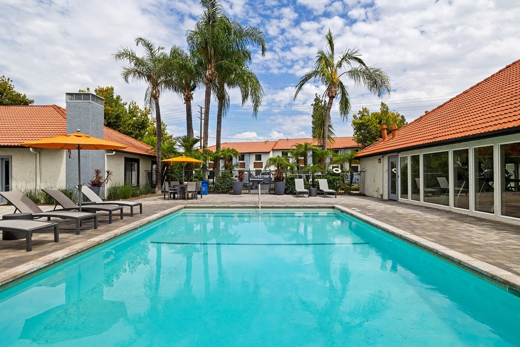 a swimming pool with chairs and umbrellas and a house in the background