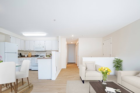 A modern kitchen with white appliances and a dining area with a white chair and table.