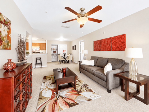 A living room with a grey couch, a brown coffee table, and a red vase on top of a wooden cabinet.