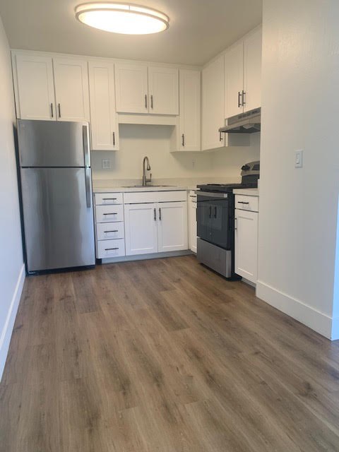 A kitchen with white cabinets and a wooden floor.at OTAVON APARTMENTS, Novato California