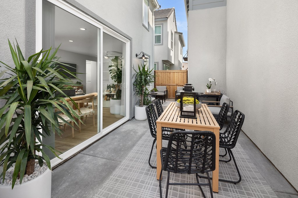 Townhouses for Rent in Roseville, CA - Solstice at Fiddyment Ranch - Spacious Patio with Table and Chairs, Area Rug, Potted Plants, Patio Chairs, and Sliding Glass Door to Interior of Apartment