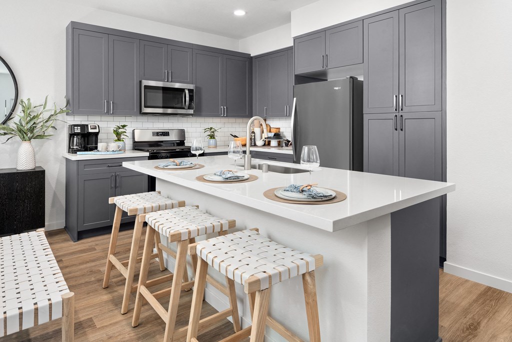 Pet-Friendly Houses for Rent in Roseville, CA - Solstice at Fiddyment Ranch - Stunning Kitchen with Wood-Style Flooring, Grey Shaker-Style Cabinets, White Tile Backsplash, Quartz Countertops, Stainless Steel Appliances, Island with Sink, and Barstools