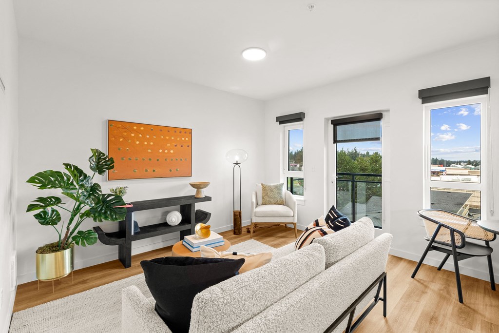 A living room with a grey sofa, a black table, a wooden coffee table, a potted plant, a painting, a lamp, a chair, and a balcony with a view of the street at Two 10 by Vintage, Washington 98133