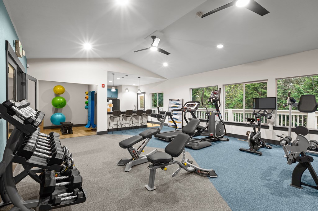 Olympia WA Apartments - Yauger Park Villas - Fitness Center with Machines, Equipment, Weights Rack, Windows, Ceiling Fans, Blue and Grey Floor, and Breakfast Bar