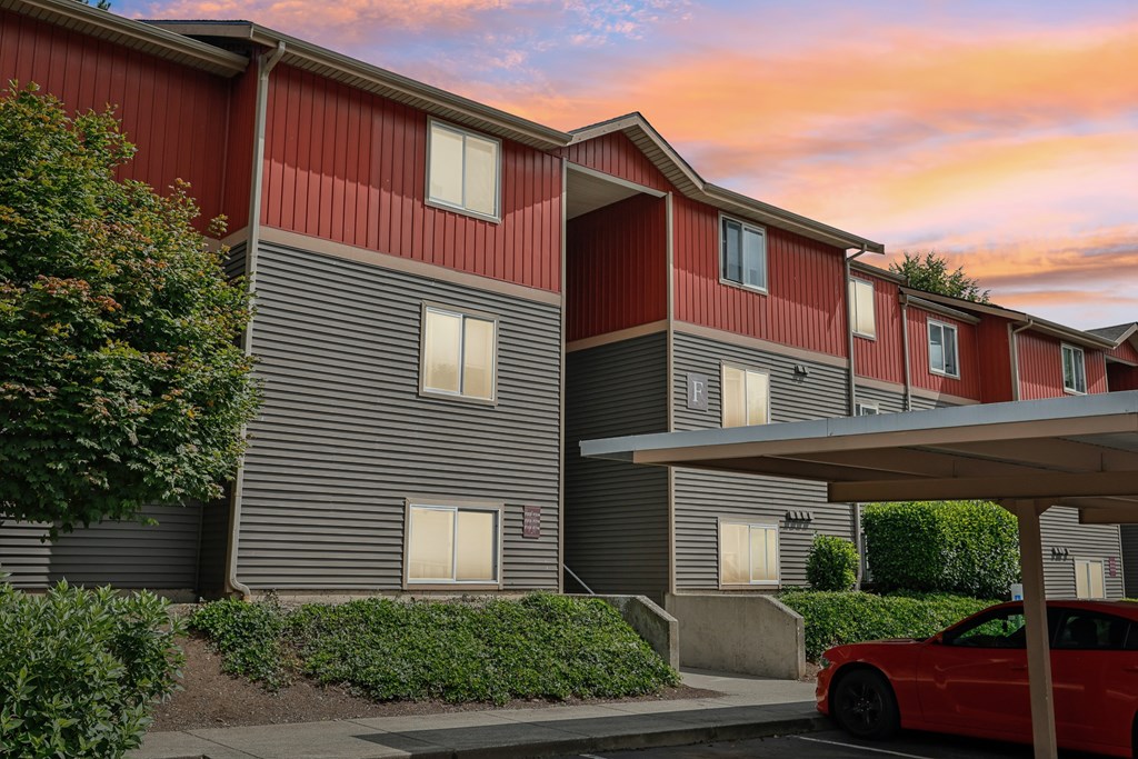 A red car is parked in front of a building with grey and red siding  at The Timbers by Vintage, Washington 98223