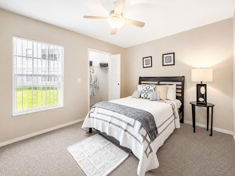 A bedroom with a bed, a ceiling fan, and a window with a view of a fence and trees.