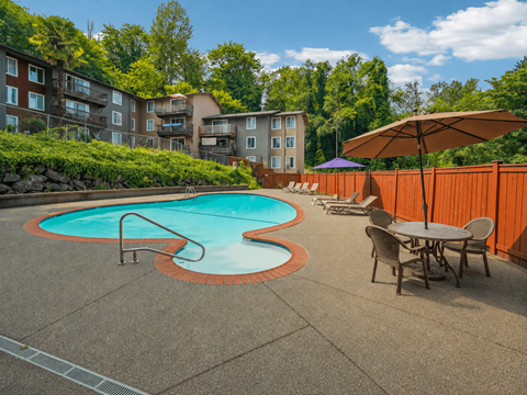 A pool surrounded by a concrete patio and chairs.