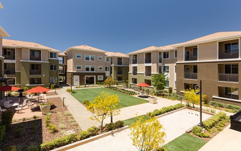an outdoor area with grass and tables and umbrellas in an apartment complex