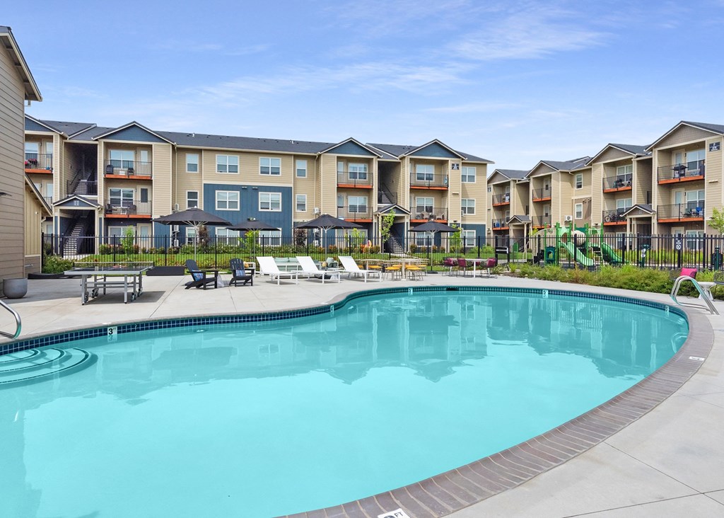 a swimming pool with lounge chairs and umbrellas in front of an apartment complex