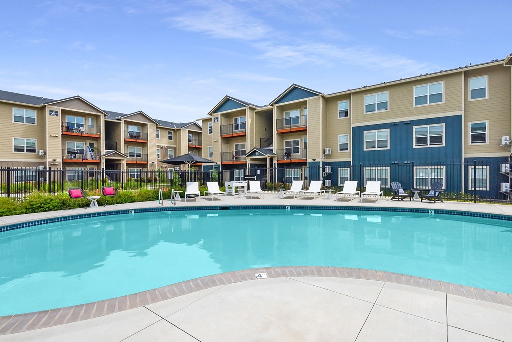 a swimming pool with lounge chairs and umbrellas in front of an apartment building