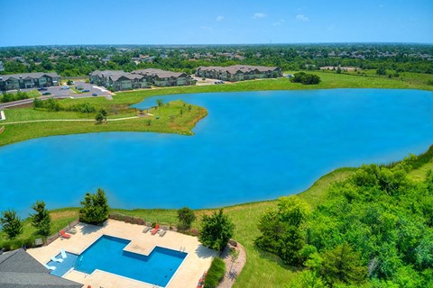 A large blue swimming pool surrounded by a grassy area and a residential neighborhood in the background.