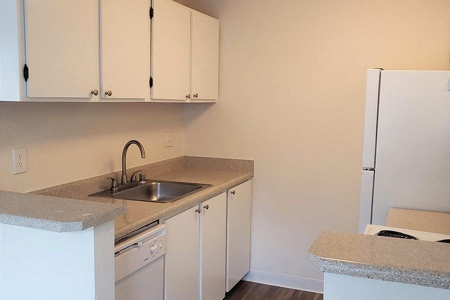 Apartments In Des Moines For Rent - Marina Club - Kitchen Area With White Cabinetry, White Appliances, Wood Plank Flooring, And Granite-Style Countertops