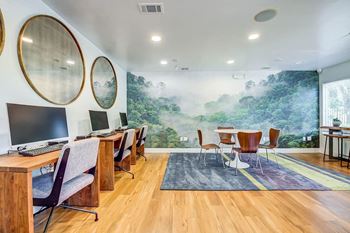 A room with a large mural of a forest on the wall and a desk with a computer and chair.