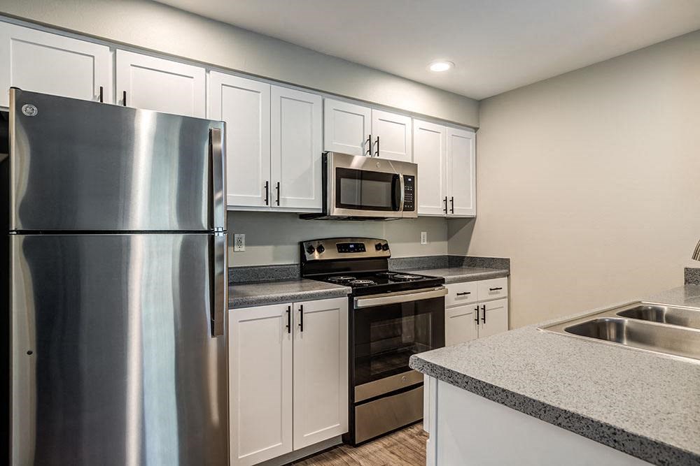 Kitchen with Stainless Appliances, Grey Countertops, White Cabinetry, and Wood-Style Flooring at BELLA SONOMA, Fife, WA
