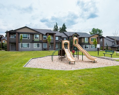 South Hill Puyallup Apartments. - Bella on Canyon - Playground Surrounded by Grass with Climbing Structure that Includes Two Slides and a Rounded Climbing Ladder