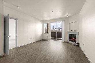 South Hill Puyallup, WA Apartments. - Bella on Canyon - Living Room with Wood-Style Flooring, Fireplace, Small Window, and Large Sliding Glass Door that Leads to a Patio - Photo Gallery