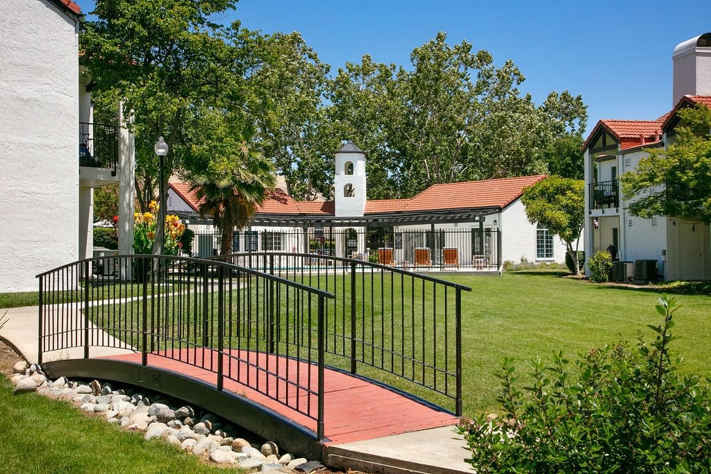 Apartment Exterior With Lush Grass, Paved Walkways With Trees and Bushes, and a Small Decorative Bridge at Laurel Creek, Fairfield, CA