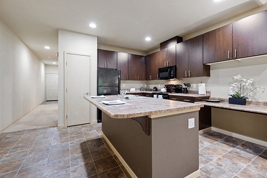 Three Bedroom Apartments in Olympia WA - Yauger Park Villas - Kitchen with Light Brown Tiled Flooring, Dark Brown Cabinetry, Black Appliances, Granite-Style Countertops, and A Large Kitchen Island.