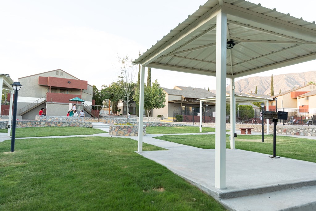 a white pavilion sits in the middle of a grassy area with houses in the background at DESERT PEAKS, EL PASO, 79912