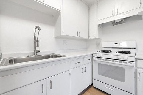 A white kitchen with a stove, sink, and cabinets.