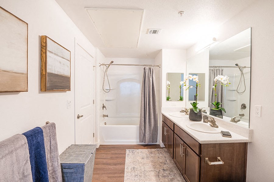 Chico, CA Apartments For Rent - Bathroom With High Ceiling, Plank Flooring, Dual Sinks, Vanity Mirror, And A Shower With Tub.