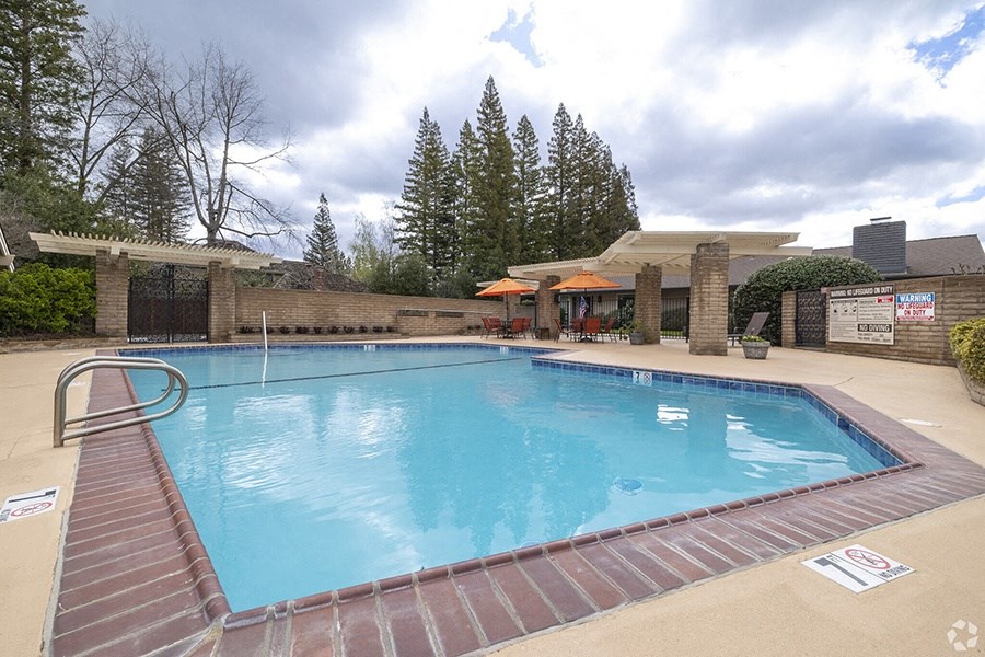 a large swimming pool with a patio and umbrellas