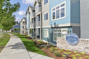 Apartments for Rent in Olympia - Briggs Village - Exterior Apartments Building with Grey and Blue Siding, Lush Greenery, and Sidewalk - Photo Gallery 3