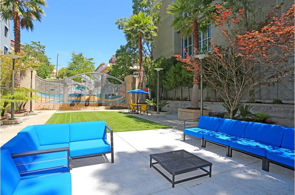a patio with blue couches and a coffee table in front of a building with a slide at K Street Flats, Berkeley, CA