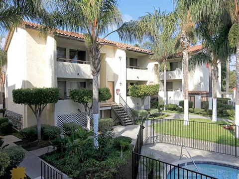 A pool is surrounded by a black fence in a sunny backyard.