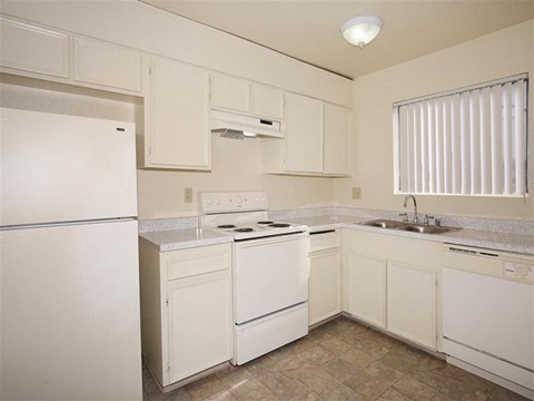 A white kitchen with a refrigerator, stove, and sink.