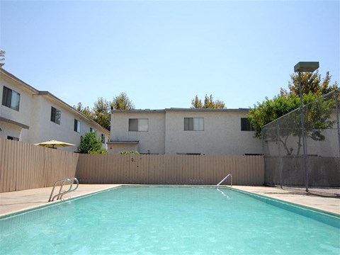 A swimming pool in front of a building with a fence and trees in the background.