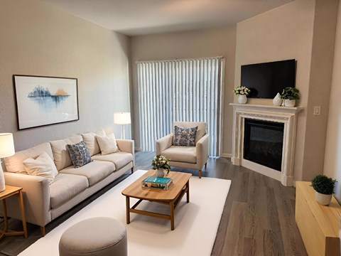 A living room with a white couch, a grey ottoman, a wooden coffee table, a fireplace, and a painting on the wall.