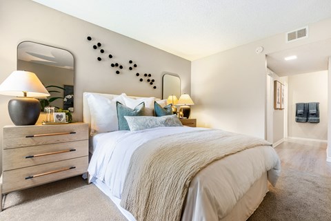 A bedroom with a large bed, a dresser with a lamp, and a mirror on the wall.